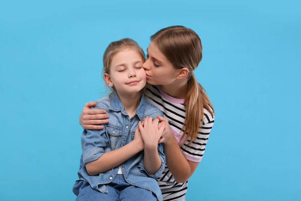 Young woman kissing her little daughter on light blue background. Happy Mother's Day - Foto, Imagem