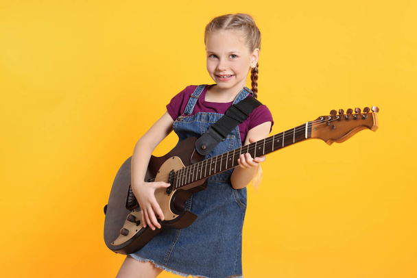Cute girl with electric guitar on orange background - Photo, image