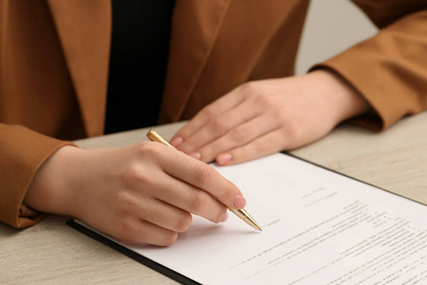 Vrouw ondertekenen document aan houten tafel, close-up - Foto, afbeelding