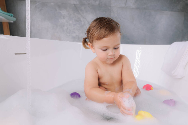 Cute little girl taking bubble bath with toys indoors - Foto, imagen