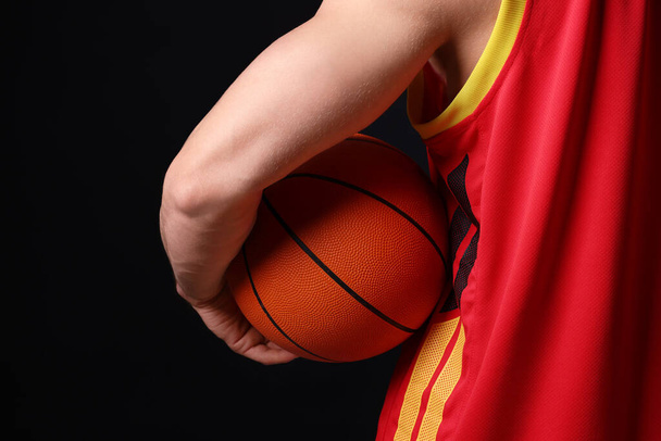 Athletic man with basketball ball on black background, closeup - Фото, изображение