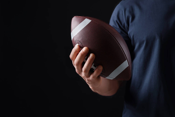 Athletic man with American football ball on black background, closeup. Space for text - 写真・画像