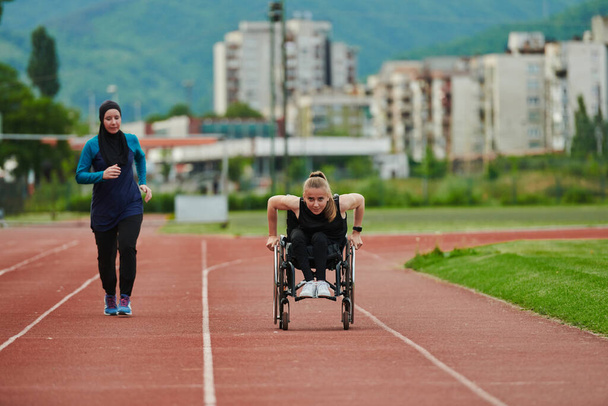 A Muslim woman in a burqa running together with a woman in a wheelchair on the marathon course, preparing for future competitions - Foto, imagen
