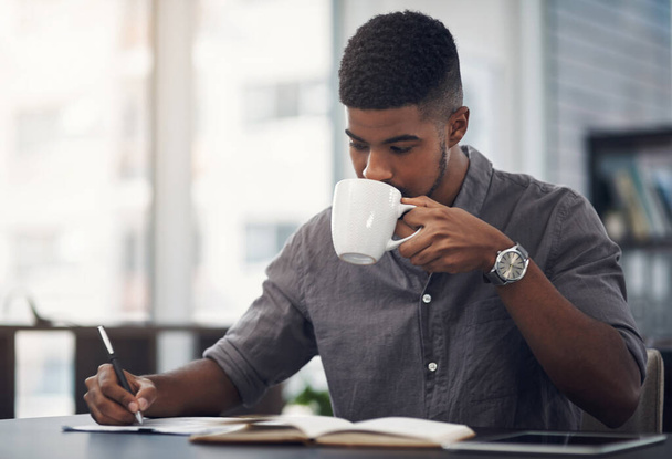 Brandstof voor een productieve werkdag. een jonge zakenman die koffie drinkt terwijl hij door papierwerk gaat in een kantoor - Foto, afbeelding