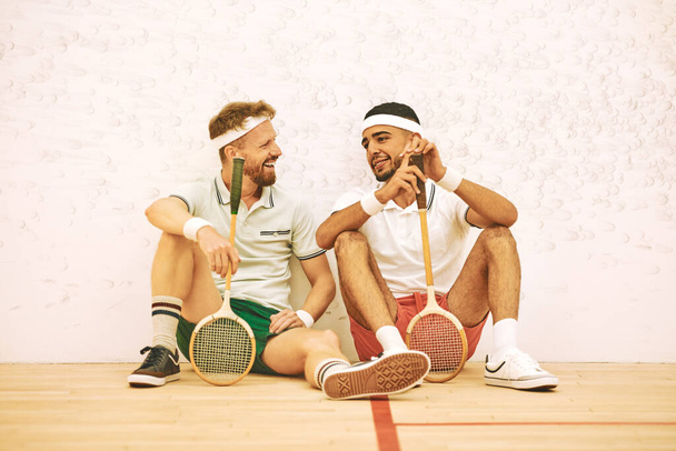 Oyunun gittikçe güzelleşiyor. İki genç adam squash oynadıktan sonra sohbet ediyorlar. - Fotoğraf, Görsel