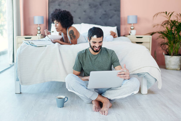 Were together and thats all that matters. a man using his laptop while sitting in the bedroom with his girlfriend - Фото, изображение