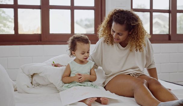 Young mother sitting on bed and drawing with her baby daughter. - Foto, imagen