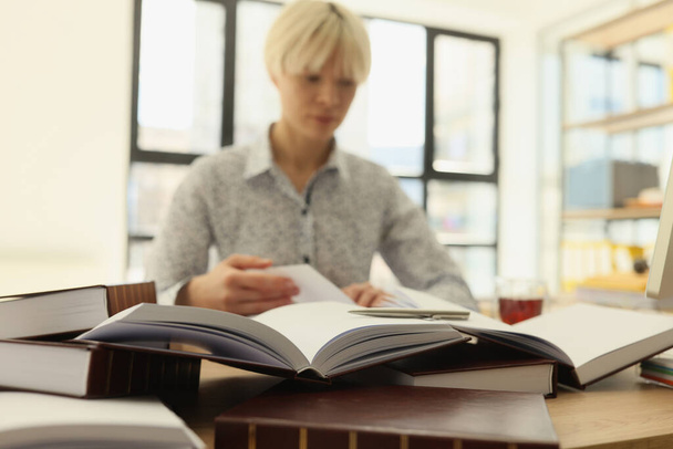 Kadın çalışanlar, profesyonel araştırmalar için kitap okurlar. Kısa sarı saçlı konsantre bir kadın ofiste oturup ders çalışıyor. - Fotoğraf, Görsel