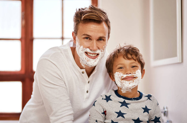 This is our idea of pampering ourselves. a man teaching his young son how to shave at home - Foto, Bild