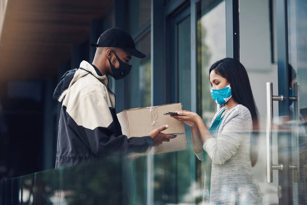 Home deliveries made safer with smart technology. a masked young man and woman using smartphones during a home delivery - Photo, Image