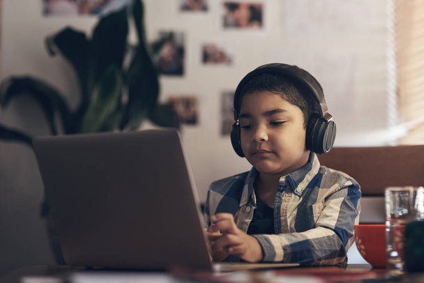 Wireless tech gave us an easier way of learning. an adorable little boy using a laptop and headphones while completing a school assignment at home - Фото, изображение