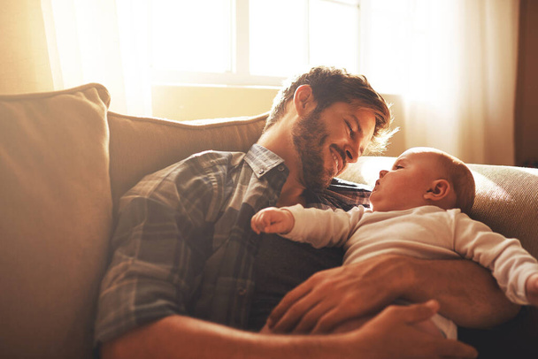 Isä, vauva ja rakkaus perheen sohvalla rakkaudella, huolenpidolla ja tuella lapselle. Onnellinen mies tai isä, jolla on hymy ja lapsi sidontaan, kehitykseen ja kasvuun tai onneen suhteessa vanhempaan. - Valokuva, kuva