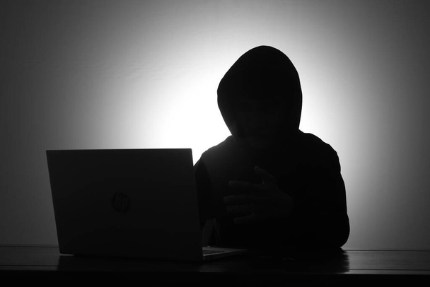 Hombre misterioso con sudadera con capucha negra usando el ordenador portátil y la celebración de la tarjeta de crédito en el cuarto oscuro. Hacker y concepto de seguridad cibernética. - Foto, Imagen