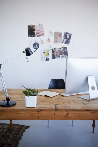 Empty office, computer desk and small business startup of interior or online marketing studio. Photo wall with desktop PC and notebook with lamp on table for creativity in a clean modern workspace. - 写真・画像