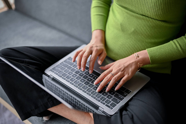 close-up image of a young Asian woman in casual clothes typing on keyboard, using her laptop computer on a sofa in her living room. work from home concept - Foto, Bild
