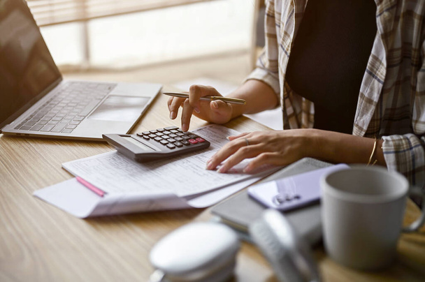 Közelkép egy nőről, aki számológépet használ, kiszámítja a pénzt, kezeli a háztartási kiadásokat és az adókat a nappaliban. - Fotó, kép