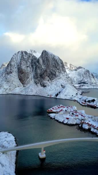 Вид с воздуха на остров Лофотен в Норвегии. Зимний сезон восхода солнца рыбацкая деревня Рейне со снежной вершиной горы размышляют о воде. Норвегия с красными домиками рорбу. С падающим снегом зимой.  - Кадры, видео