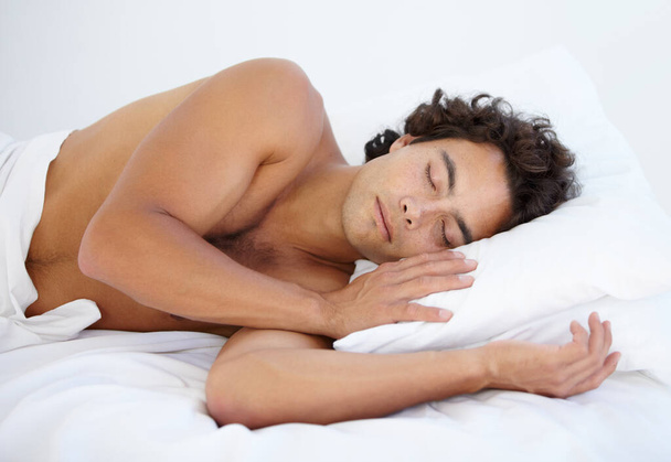 Odpočiň si, v klidu a muž spí o víkendu ráno v posteli s načechraným polštářem u sebe doma. Relaxujte, poklidný a mužský člověk si zdřímne a sní v ložnici svého domova nebo bytu - Fotografie, Obrázek