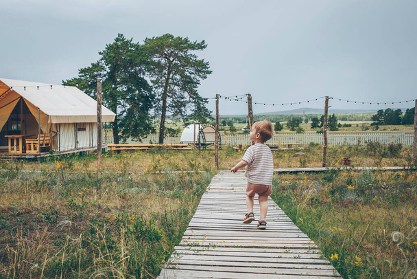 Niño de 2-3 años corriendo por un sendero de madera en un camping. Camping y vacaciones concepto al aire libre - Foto, imagen