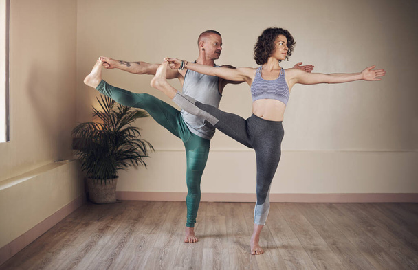 Praktizieren Sie Yoga, um besser zu leben. Aufnahme in voller Länge von zwei jungen Yogis, die zusammen stehen und eine Yoga-Pose während einer Sitzung im Innenraum halten - Foto, Bild