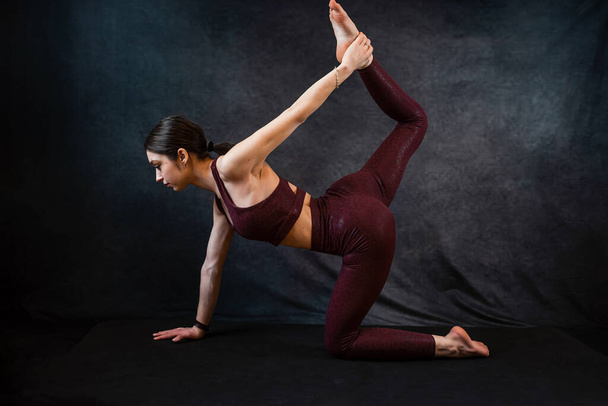 Caucasian slim girl in red sportswear make morning stretching exercises at blackstudio background. Fitness as active lifestyle - Valokuva, kuva