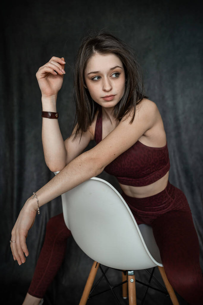 Athletic brunette young woman wear clort bra sitting on chair at studio shoot. Sporty lifestyle - Fotografie, Obrázek