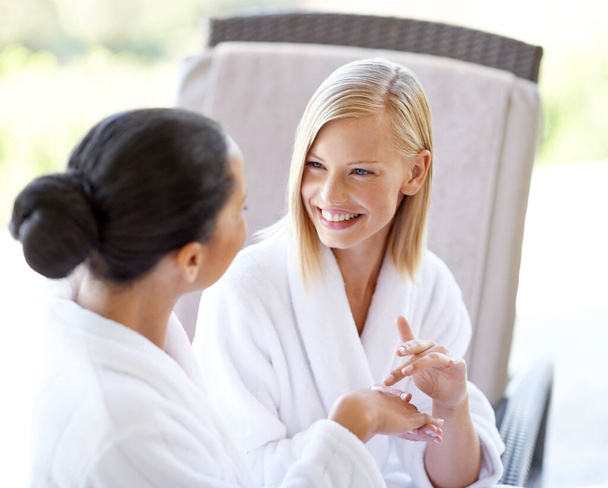 Happy, talking and friends with cream at a spa for hands, treatment and wellness of skin. Smile, skincare and women speaking while applying lotion for moisture, smooth and soft hand at a salon. - Foto, imagen