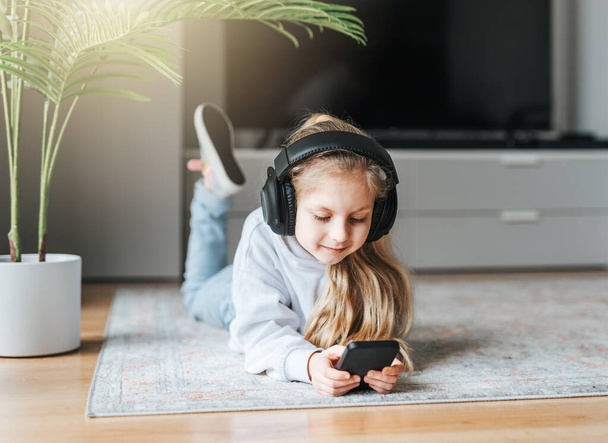 Smiling little girl listening music lying on the floor - Фото, зображення