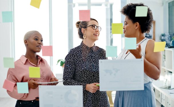 Pläne schmieden, während sie Maßnahmen zur Erreichung ihrer Ziele ergreifen. eine Gruppe von Geschäftsfrauen beim Brainstorming mit Zetteln an einer Glaswand in einem Büro - Foto, Bild