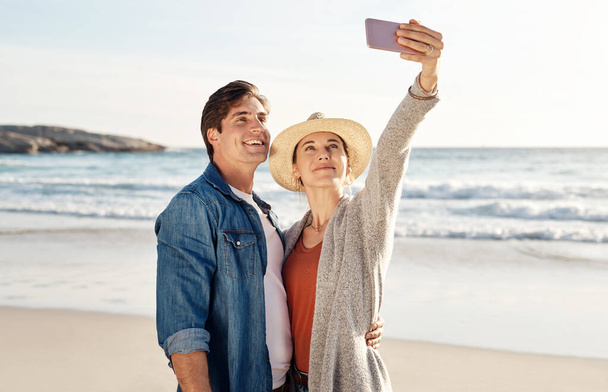 Les selfies de plage sont les meilleurs. un couple d'âge moyen prenant un selfie sur la plage - Photo, image