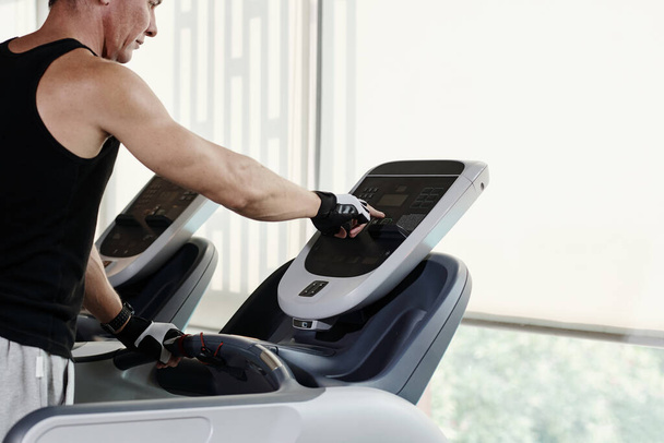 Homme mûr fixant la vitesse sur le tapis roulant lors de l'exercice dans la salle de gym - Photo, image