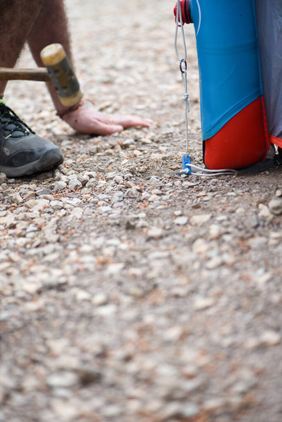 detail van man 's hand en voet rijden pikhouweel in de grond voor het opzetten van tent op de camping, harde aarde en steen camping - Foto, afbeelding