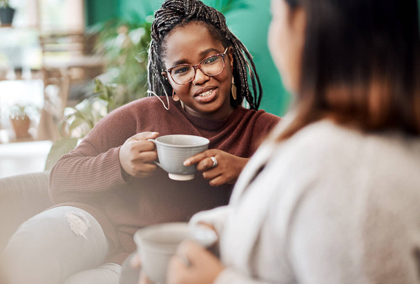 コーヒー、女子会の公式ドリンク。2人の若い女性がコーヒーを飲みながら家でソファでおしゃべりし - 写真・画像