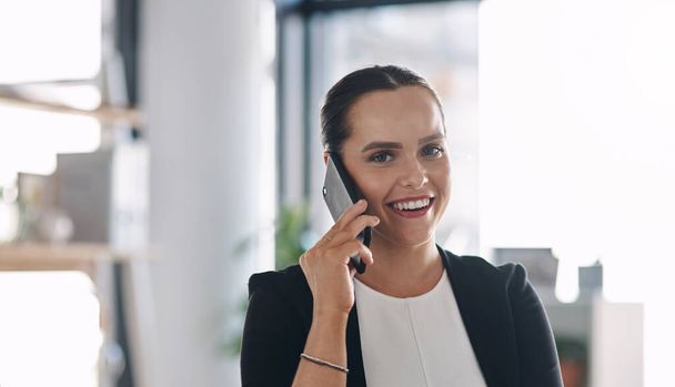 Hearing good news always puts a smile on my face. Portrait of an attractive young businesswoman answering a phone call inside her office - Photo, image