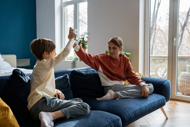 Happy children siblings giving high five to each other while playing together at home, older sister spending time with younger brother, sitting on sofa in living room and having fun - Fotoğraf, Görsel