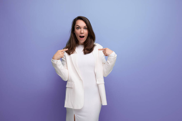 happy lucky brunette woman in ivory jacket and white dress on purple background with copy space. - Photo, Image