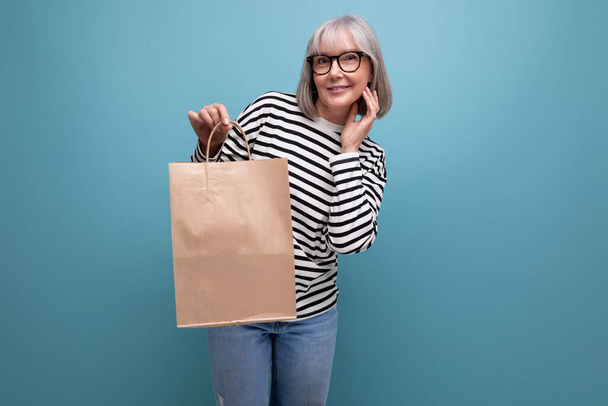 adorable mujer de mediana edad sosteniendo embalaje artesanal para ir de compras sobre fondo brillante con espacio de copia. - Foto, Imagen