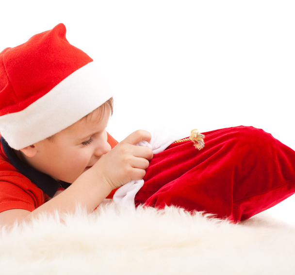 Boy in Santa's hat open christmas bag with gifts - Фото, изображение