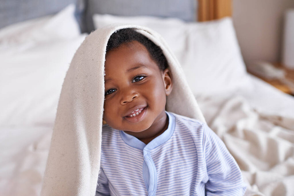Портрет, счастливый и ребенок с одеялом в постели, просыпаясь и играя в своем доме. Милый, улыбчивый и африканский мальчик-малыш в спальне симпатичный, веселый и сладкий, милый и игривый во время отдыха. - Фото, изображение