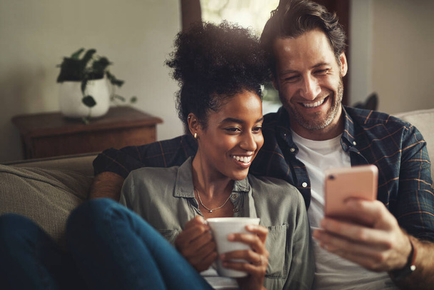 Regarde ces messages avec moi. un jeune couple heureux utilisant un téléphone portable ensemble tout en se relaxant sur un canapé à la maison - Photo, image