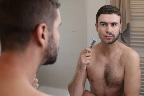 portret van knappe jongeman met half geschoren baard voor spiegel in badkamer - Foto, afbeelding