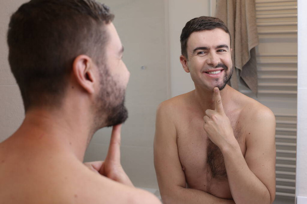 retrato de joven guapo con barba medio afeitada delante del espejo en el baño - Foto, Imagen