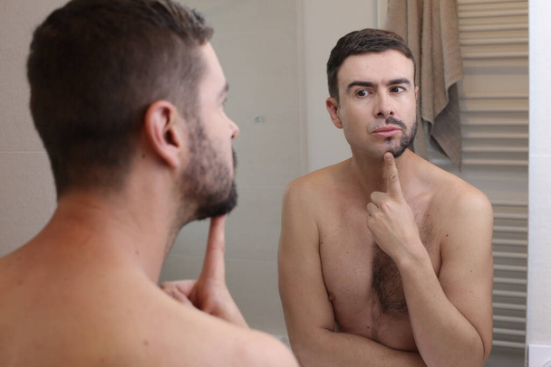 retrato de joven guapo con barba medio afeitada delante del espejo en el baño - Foto, Imagen