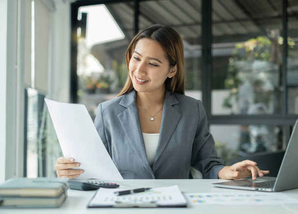Asiatische Geschäftsfrau sitzen an ihrem Schreibtisch und berechnen Finanzgrafiken, die Ergebnisse ihrer Investitionen zeigen, planen einen erfolgreichen Geschäftsprozess. - Foto, Bild