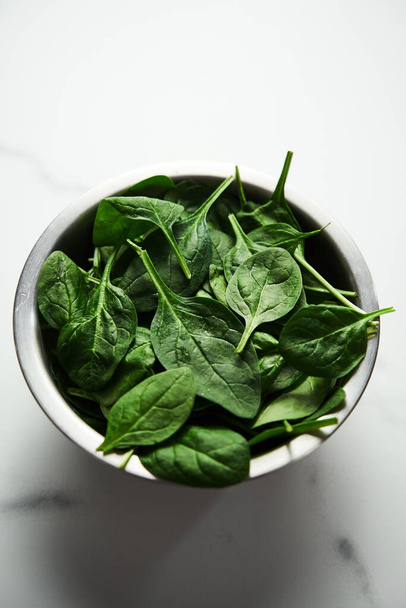 A bunch of Fresh baby spinach leaves in the in a stainless steel bowl on white marble background. High quality photo - Zdjęcie, obraz