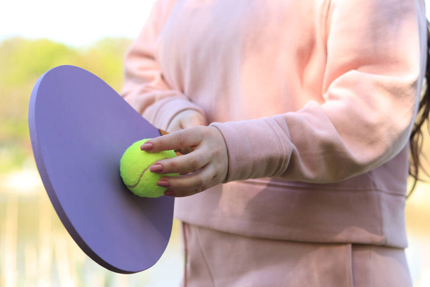 Las manos de las mujeres con una raqueta de madera y una bola verde de cerca. Deportes al aire libre actividad de ocio - Foto, imagen