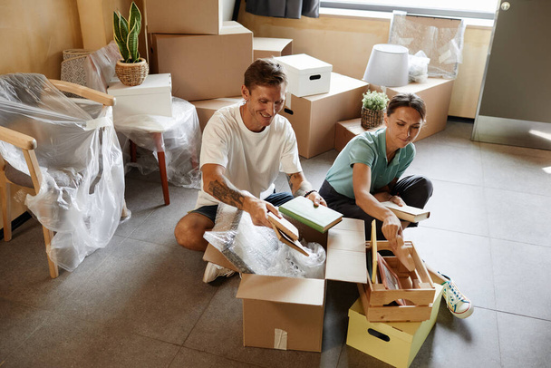 Portrait of tattooed couple unpacking cardboard boxes sitting on floor while moving into new house, copy space - Photo, Image