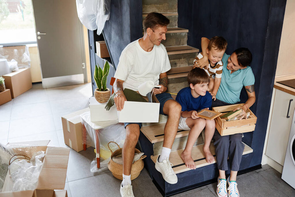 Portré boldog modern család kipakolás dobozok, miközben ül a lépcsőn az új otthon és mosolygós, másolja a helyet - Fotó, kép