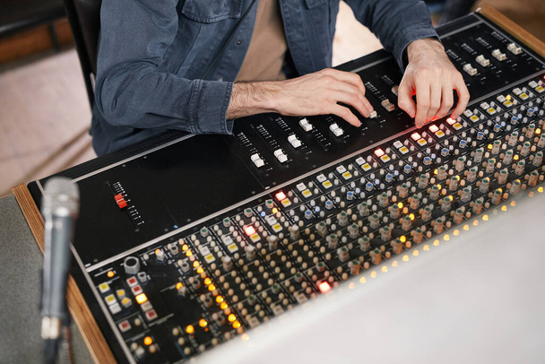 Close up of unrecognizable man operating buttons and toggles at audio workstation in professional recording studio, music producer - Φωτογραφία, εικόνα