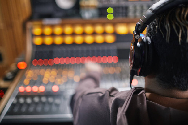 Visão traseira no jovem músico usando fones de ouvido na estação de trabalho de áudio em estúdio de gravação profissional, espaço de cópia - Foto, Imagem